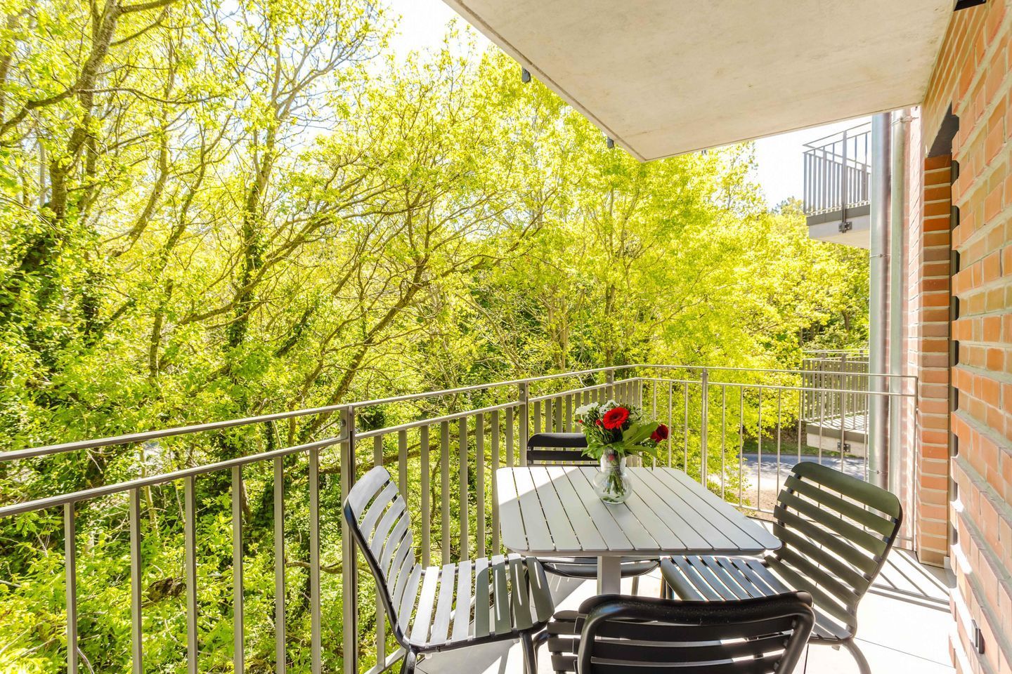 Ein Balkon mit Tisch und Stühlen, einer Blumenvase und Blick auf Bäume.