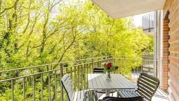 Ein Balkon mit Tisch und Stühlen, einer Blumenvase und Blick auf Bäume.