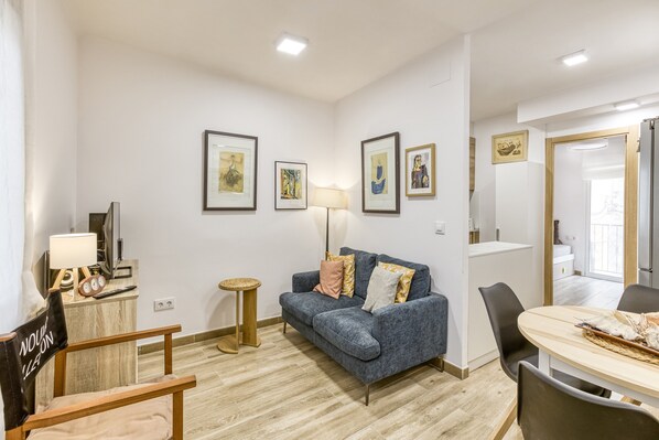 Een woonkamer met een bank, een eettafel, een lamp en kunstwerken in lijsten aan de muren.