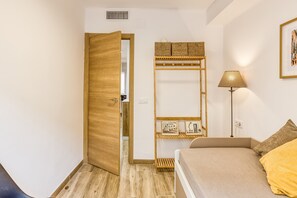 Een slaapkamer met een houten kledingkast, een nachtkastje met een lamp en een bed met een geel kussen.