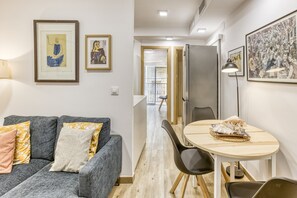A modern living room with a grey sofa, a dining table with chairs, and framed artwork on the walls.