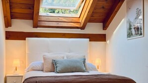 Un dormitorio con techo de madera, una cama con colcha marrón, dos lámparas de noche y un cuadro en la pared.