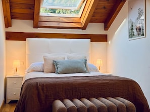 A bedroom with a wooden ceiling, a bed with a brown bedspread, two bedside lamps, and a framed picture on the wall. - Valle de Camaleño Apartamentos (Camaleno)