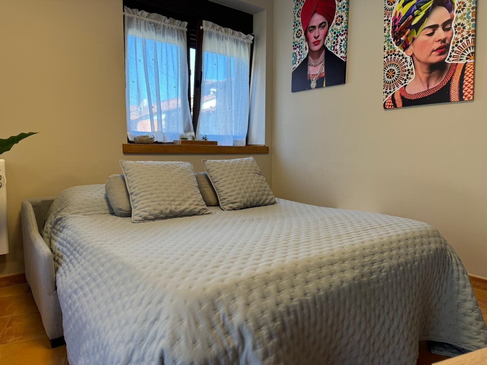 A bedroom with a bed, pillows, a window with curtains, and a wall with a framed picture.