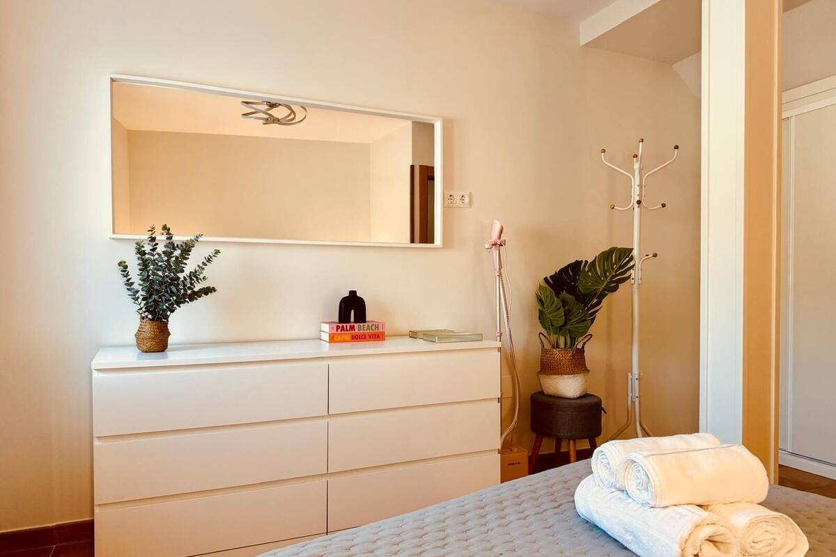 Un dormitorio con cama, cómoda, espejo, perchero y planta en maceta.