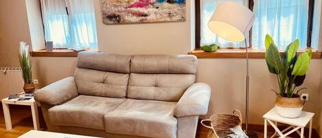 A living room with a beige sofa, a white coffee table, a floor lamp, a painting, and a window with curtains.
