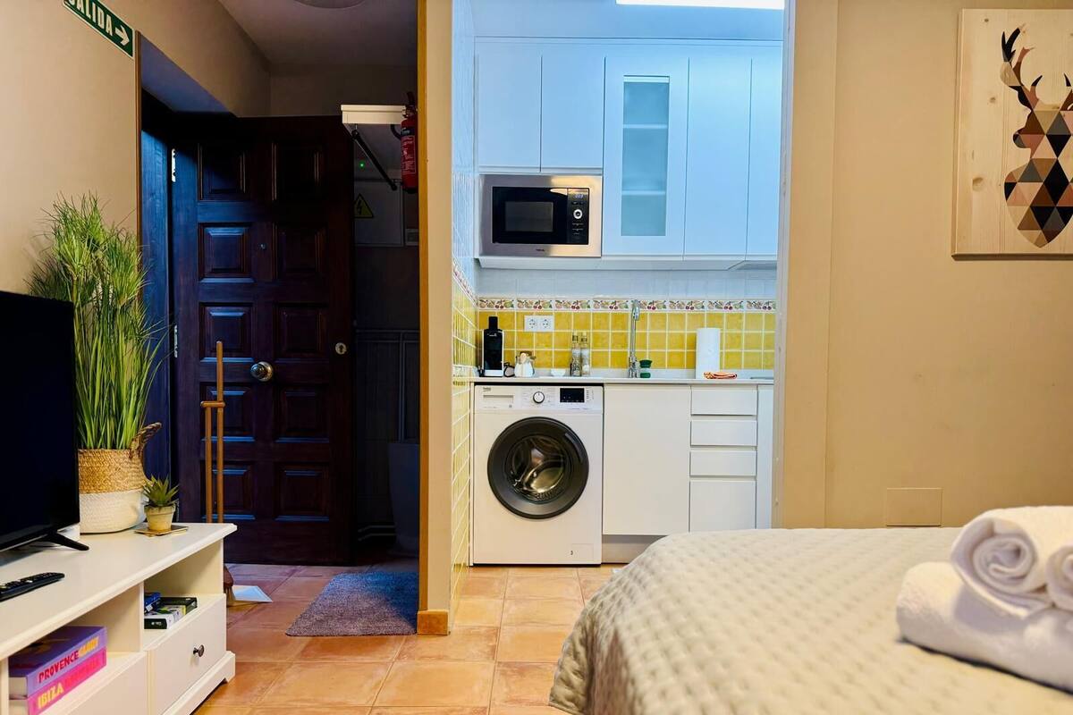 Una habitación funcional con cama, lavadora, microondas y pequeña cocina.