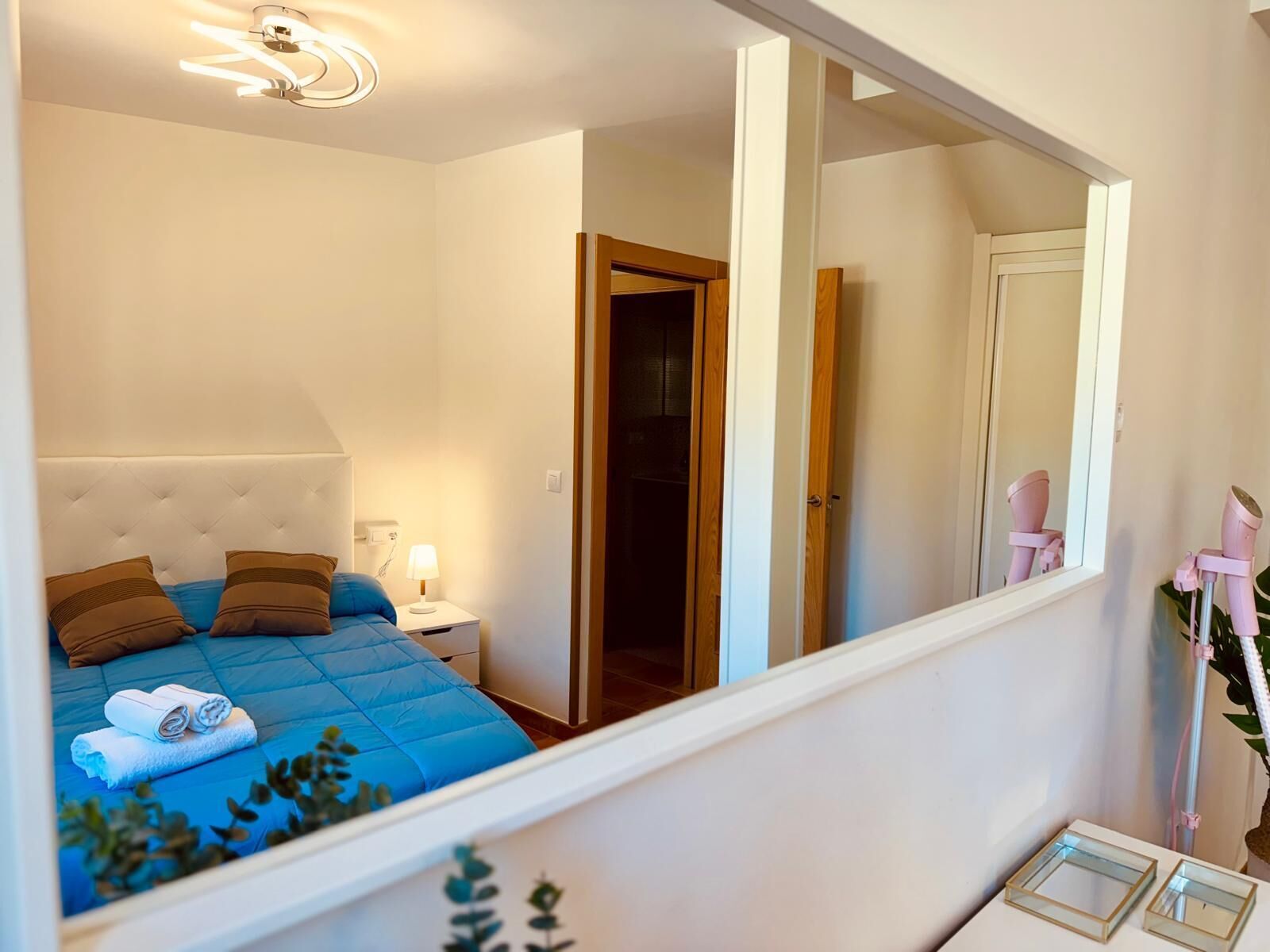 A bedroom with a bed, bedside lamp, and a mirror reflecting the room.