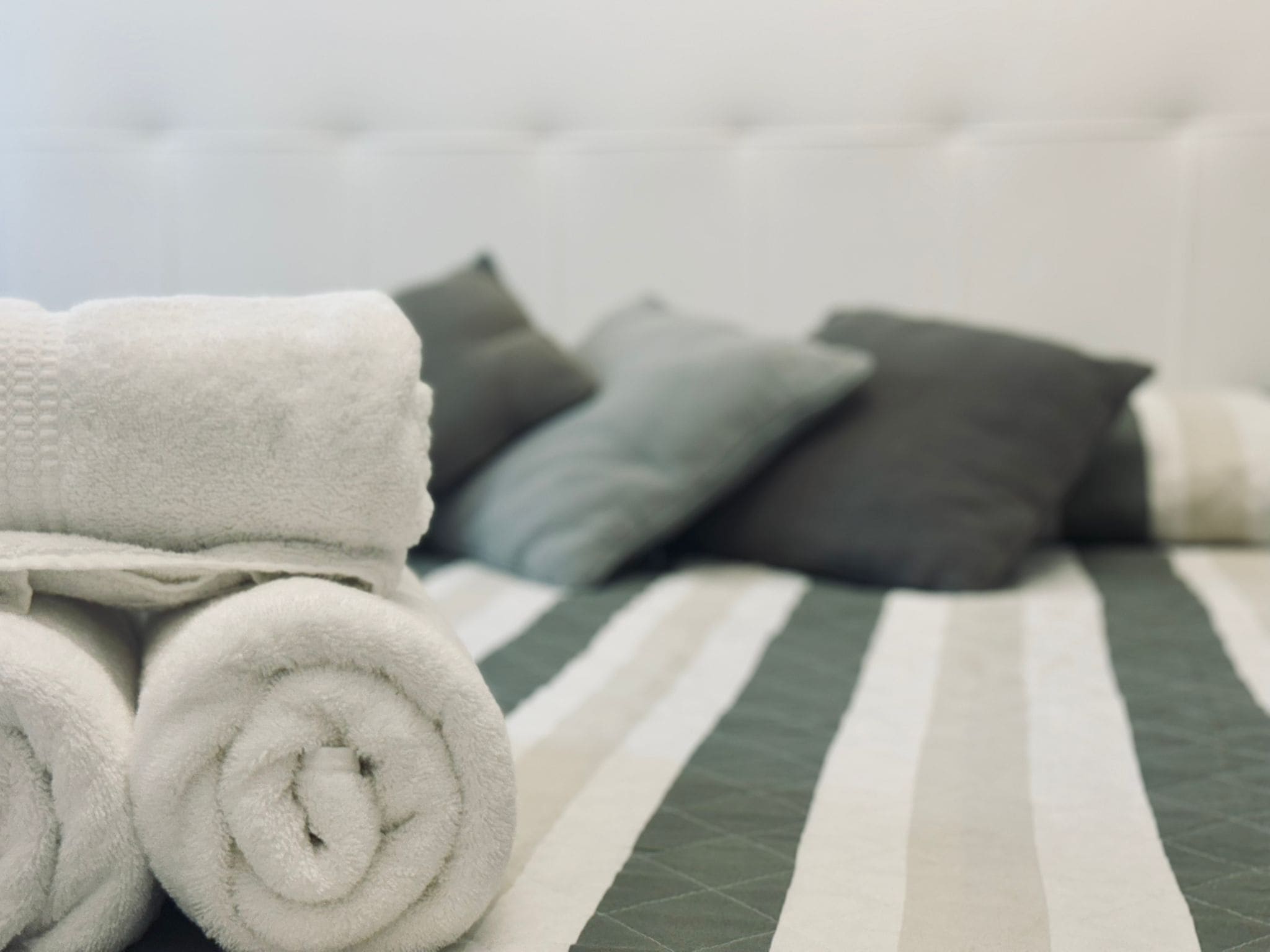 A neatly made bed with rolled white towels and grey pillows.