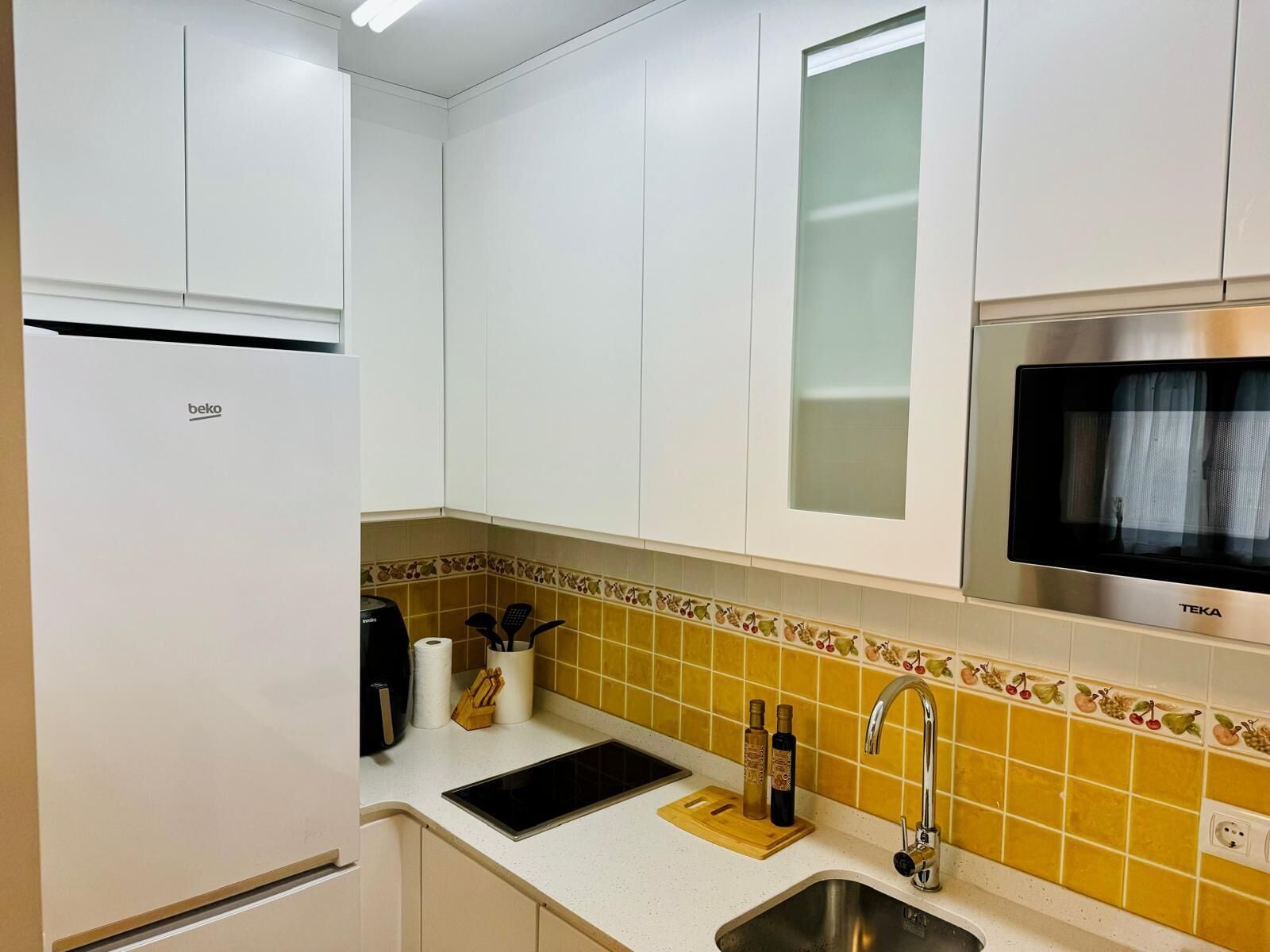 A kitchen with white cabinets, a built-in microwave, a sink, and a countertop with a cutting board and kitchen utensils.