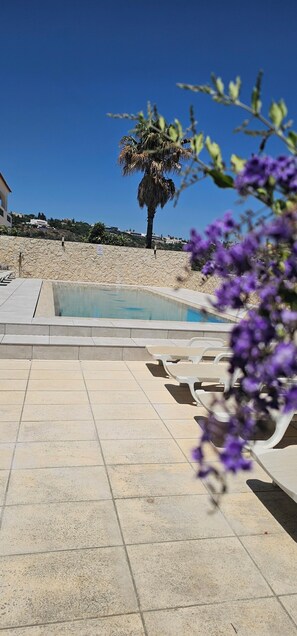 A pool area with lounge chairs, a palm tree, and a stone wall. - Exceptional villa, infinity pool, view of the marina and cliffs, close to beaches. (Albufeira)
