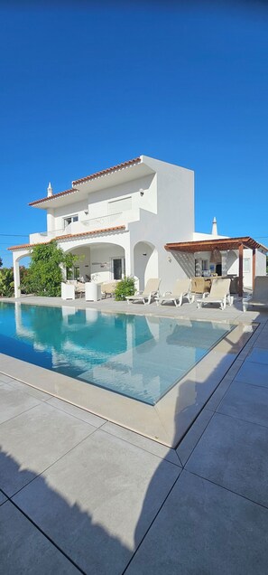 Un bâtiment moderne de couleur blanche, doté d’une piscine, d’un espace extérieur aménagé et d’une zone couverte.