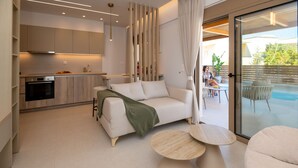 Ein modernes Wohnzimmer mit einer Couch, zwei runden Tischen, einer Küche im Hintergrund und einer Glastür, die zu einem Außenbereich führt.