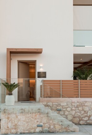 A modern building entrance with a wooden door, a stone wall, and a potted plant. - Casa Doma Luxury Suite with Heated Mini Pool and Private Parking (Rethymno Town)