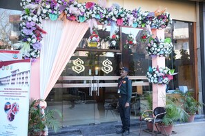 A hotel entrance with a sign, a security guard, and a floral decoration. - Hotel Samdariya Gold Rewa (Huzur)