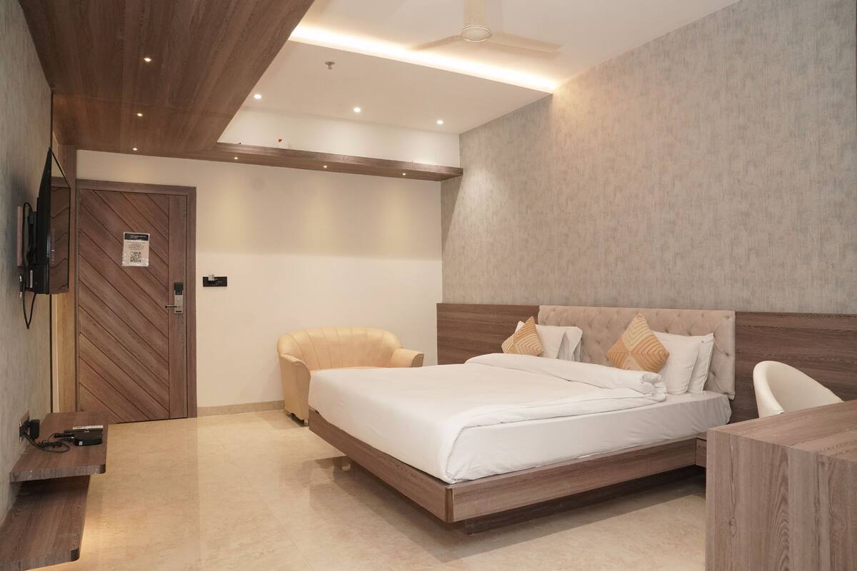 Ein Schlafzimmer mit Bett, Stuhl, Schreibtisch, Holztür und einem an der Wand befestigten Fernseher.