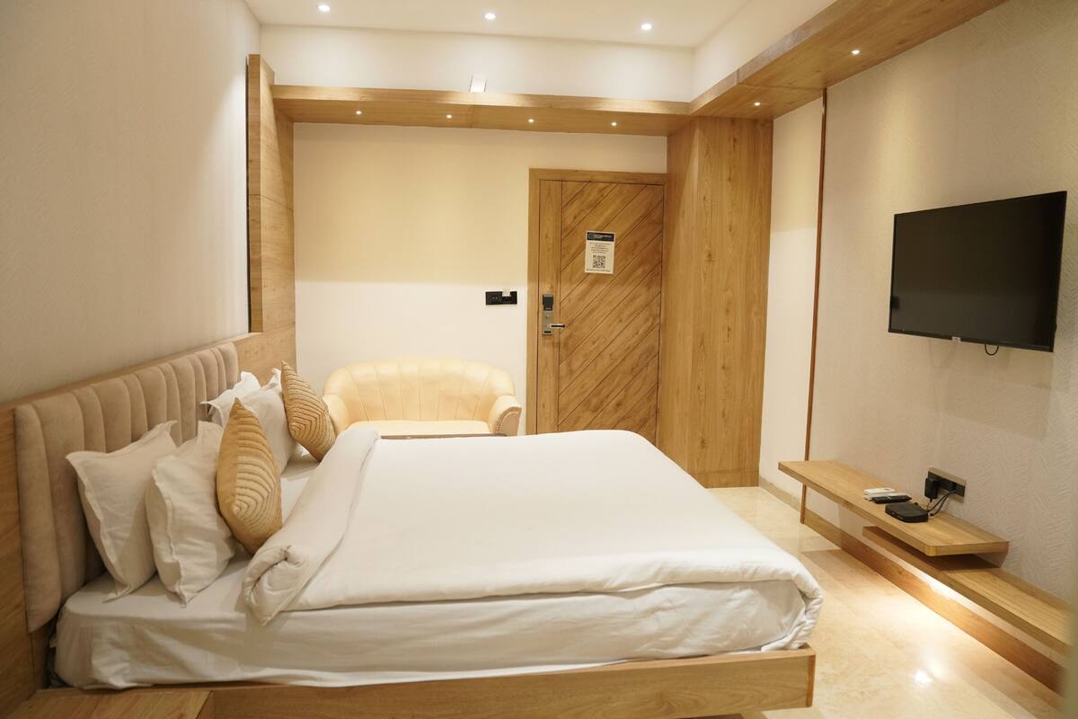 Ein modernes Hotelzimmer mit einem großen Bett, einem hölzernen Kopfteil, einem Fernseher und einer Holztür.