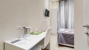 Una camera d'albergo con una scrivania, un letto, una TV a parete e una finestra con tende.