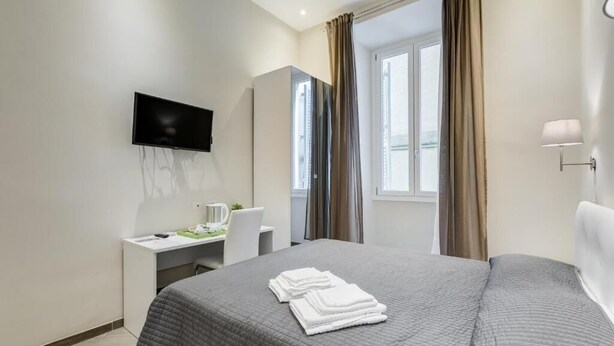 Una camera d'albergo con un letto, una scrivania, una televisione e una finestra con tende.