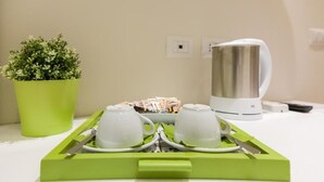 Un vassoio con due tazze bianche, una pianta verde e un bollitore bianco su una superficie chiara.
