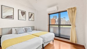 Een hotelkamer met twee bedden, een groot raam met uitzicht op gebouwen en een airconditioning.