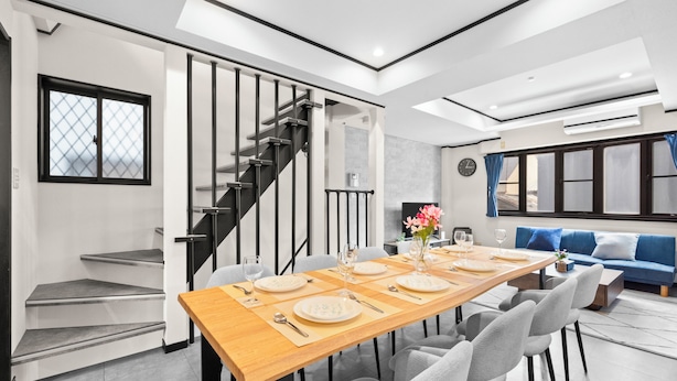 Een moderne eethoek met een houten tafel gedekt voor vier personen, een trap en een blauwe bank op de achtergrond.