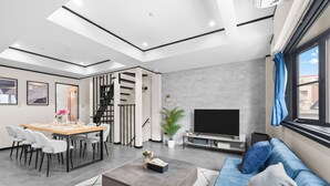 Een moderne woonkamer met een eethoek, een zithoek, een flatscreen televisie en een trap.