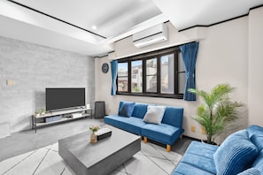 A modern living room with a sofa, a coffee table, a TV, and a potted plant. - Smart Stay Inn EbisuNishi (Osaka)