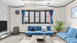 Een moderne woonkamer met een blauwe bank, een salontafel, een televisie en een groot raam met gordijnen.