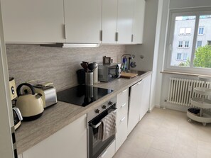 Eine moderne Küche mit weißen Schränken, einer schwarzen Induktionskochplatte, einem Wasserkocher, einem Toaster und einem Spülbecken mit Fenster darüber.