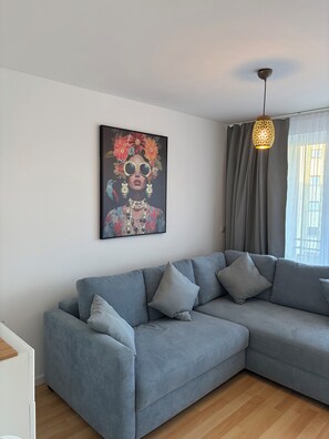 Un salon moderne avec un canapé d’angle gris, un élément décoratif mural et un luminaire suspendu.