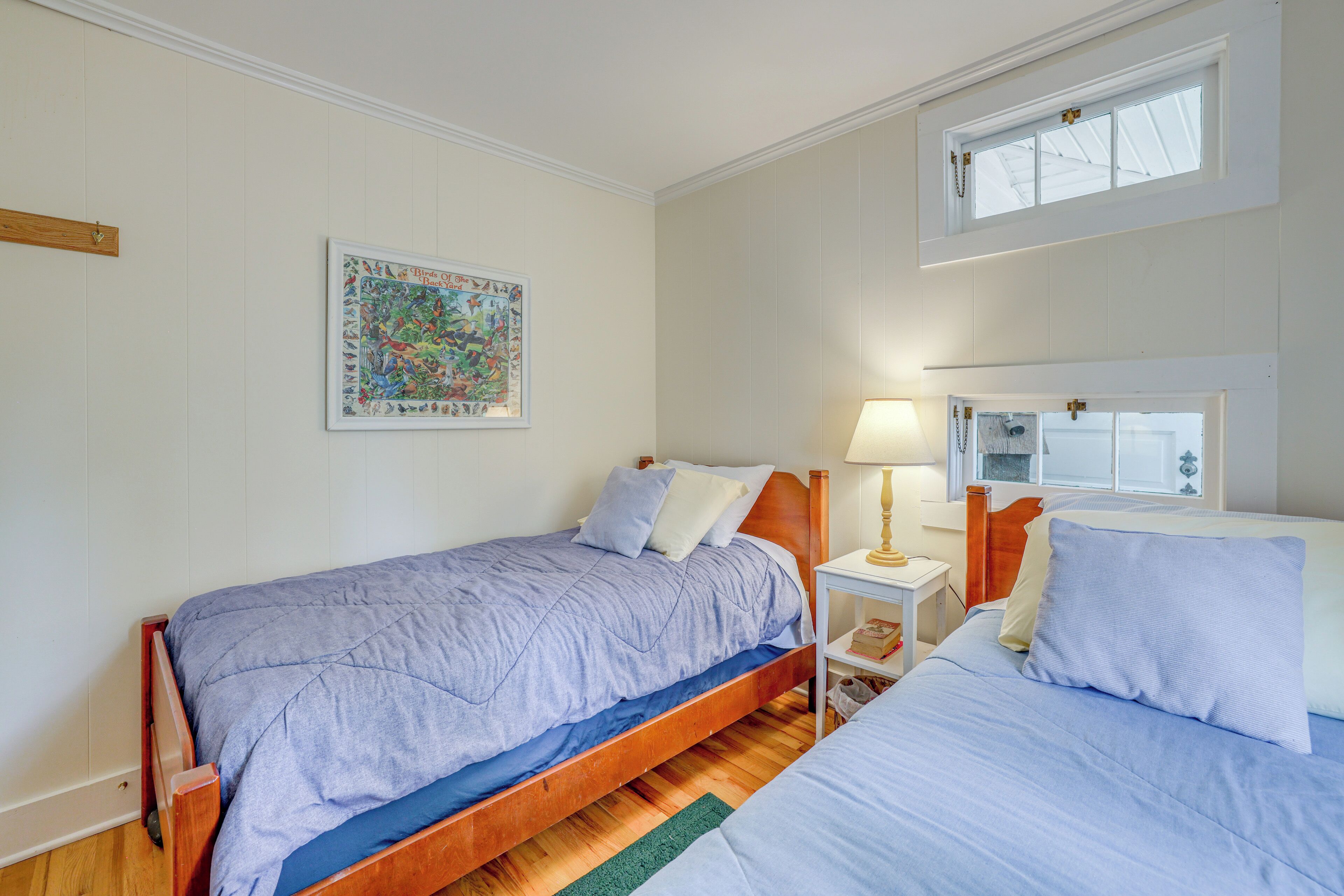 A bedroom with two beds, a nightstand, a lamp, a framed picture, and a window.