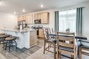 A modern kitchen with wooden cabinets, a central island, bar stools, and a dining table with chairs. - Spacious & Modern! New Home Near Gaylord Rockies (Aurora)