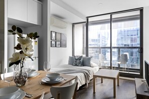 A modern hotel room with a large bed, a dining table set for two, and a view of the city through large windows. - Stylish Pet-friendly 2br, Walk to Southern Cross (Melbourne)