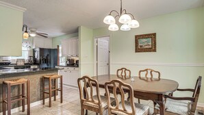 Un coin repas avec une table et des chaises en bois, une cuisine à l’arrière-plan et un ventilateur de plafond.