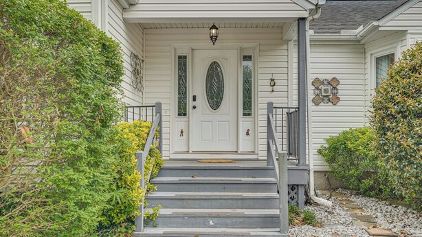 Une maison avec une porte d’entrée blanche, un petit porche et des marches menant à l’entrée.