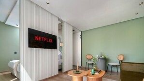 Una sala de estar moderna con un televisor de pantalla plana en la pared, un sofá, dos sillones, una mesita redonda y un jarrón decorativo.