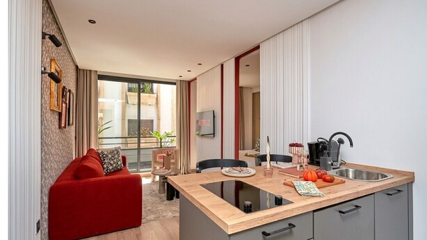 Cocina moderna con una isla central, zona de comedor con un sofá rojo y vistas al exterior.
