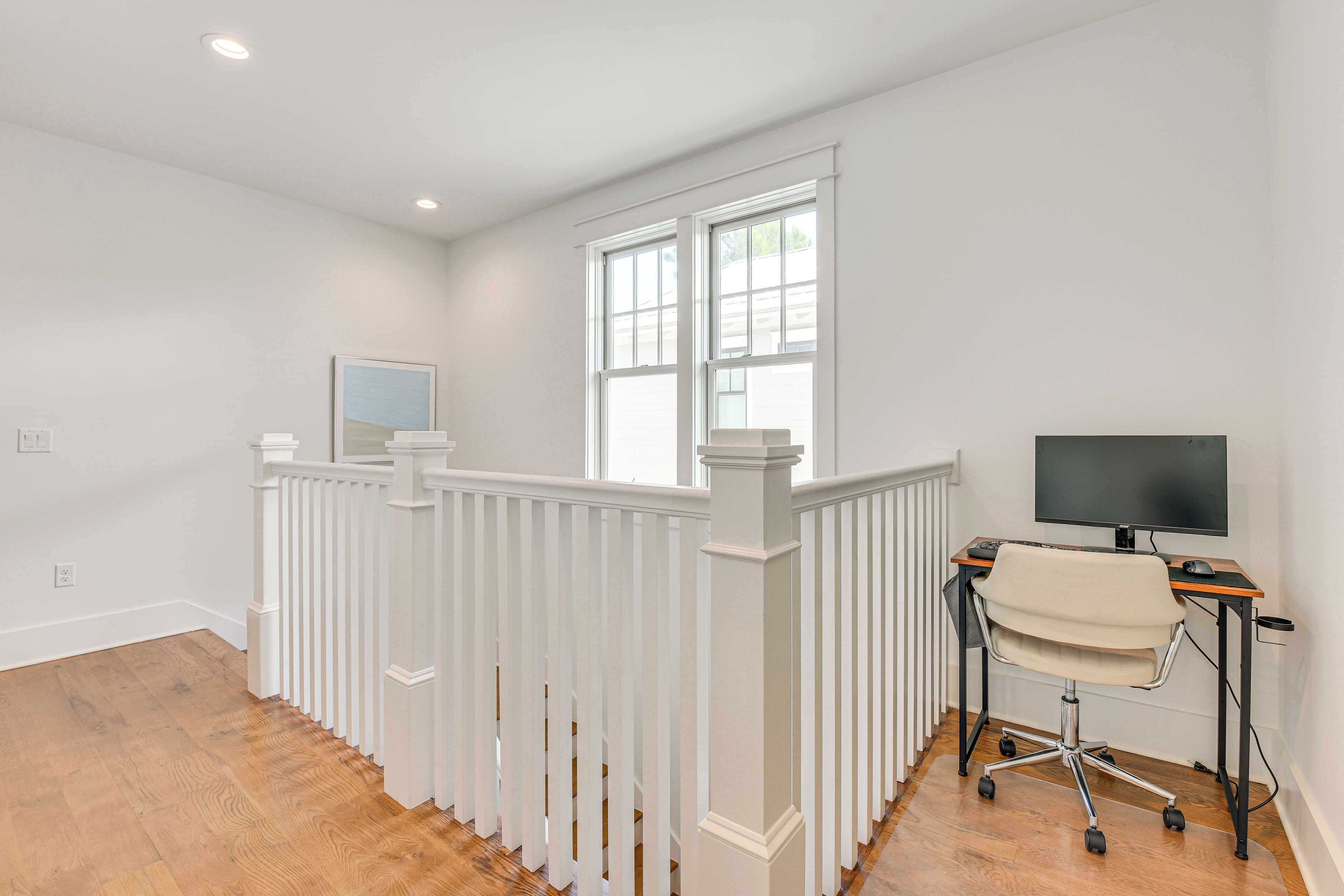 Une pièce avec une rambarde blanche, un bureau avec une chaise, une télévision et une fenêtre.