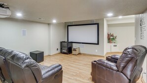 Una sala de cine en casa con dos sillones de cuero reclinables, un televisor de pantalla plana grande, un proyector y un altavoz.