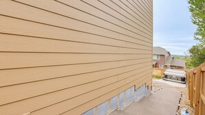 Un edificio residencial con revestimiento horizontal, un sendero de hormigón y una valla de madera.