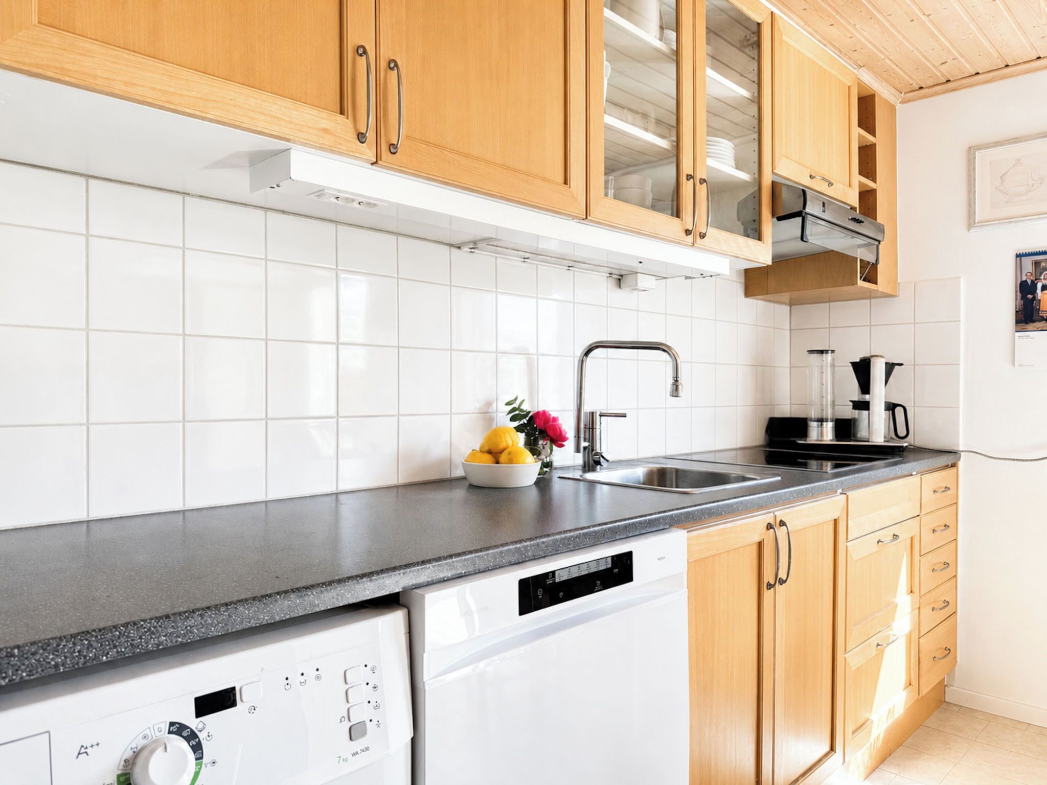Una cocina moderna con armarios de madera, lavavajillas, pileta y una mesada con cafetera.