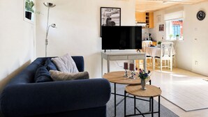 Een moderne woonkamer met een bank, een televisie, een klein tafeltje met kaarsen, en een keuken op de achtergrond.