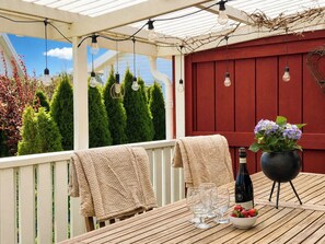 A wooden deck with a table set for dining, a bottle of wine, and a bowl of strawberries. - Skeaberg by Interhome (Halmstad)