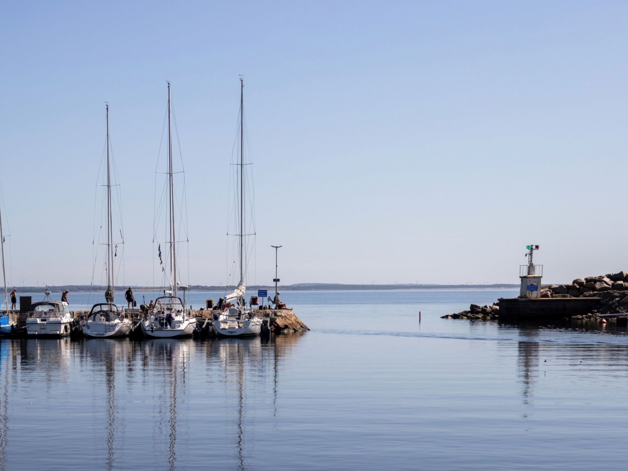 Un port de plaisance où sont amarrés plusieurs voiliers, un phare et une eau calme.