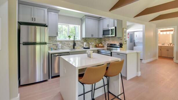 Een moderne keuken met roestvrijstalen apparatuur, een centraal eiland met barkrukken en een uitzicht op de aangrenzende eetruimte.