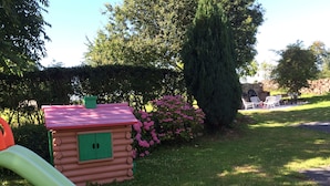 Une cabane en rondins avec un toit rouge, un toboggan et des fleurs roses à proximité.