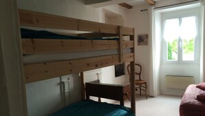 Un lit superposé avec un bureau et une chaise, une fenêtre avec des rideaux et un radiateur.