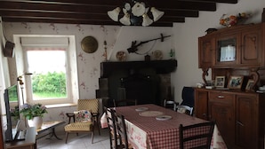 Un coin repas avec une nappe à carreaux, des chaises en bois, une cheminée et une fenêtre donnant sur un paysage verdoyant.