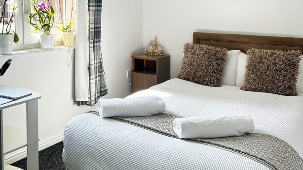 Un dormitorio con cama, una mesita de noche, cortinas en la ventana y una obra de arte en la pared.